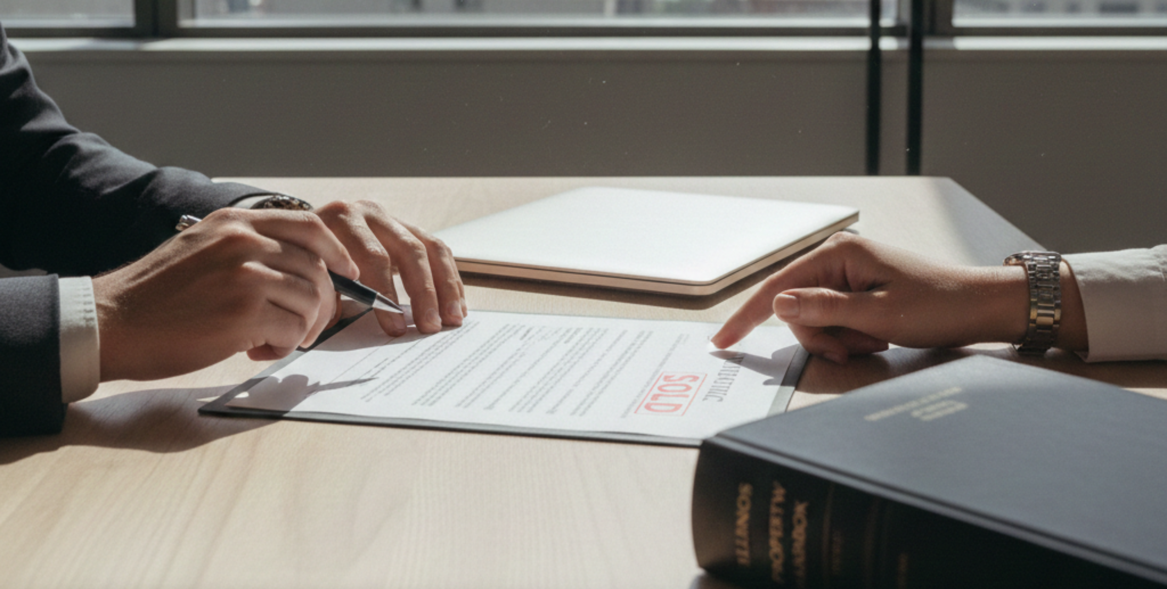Faceless view of hands reviewing a Chicago real estate contract on a desk, with documents, laptop, and law book visible.
